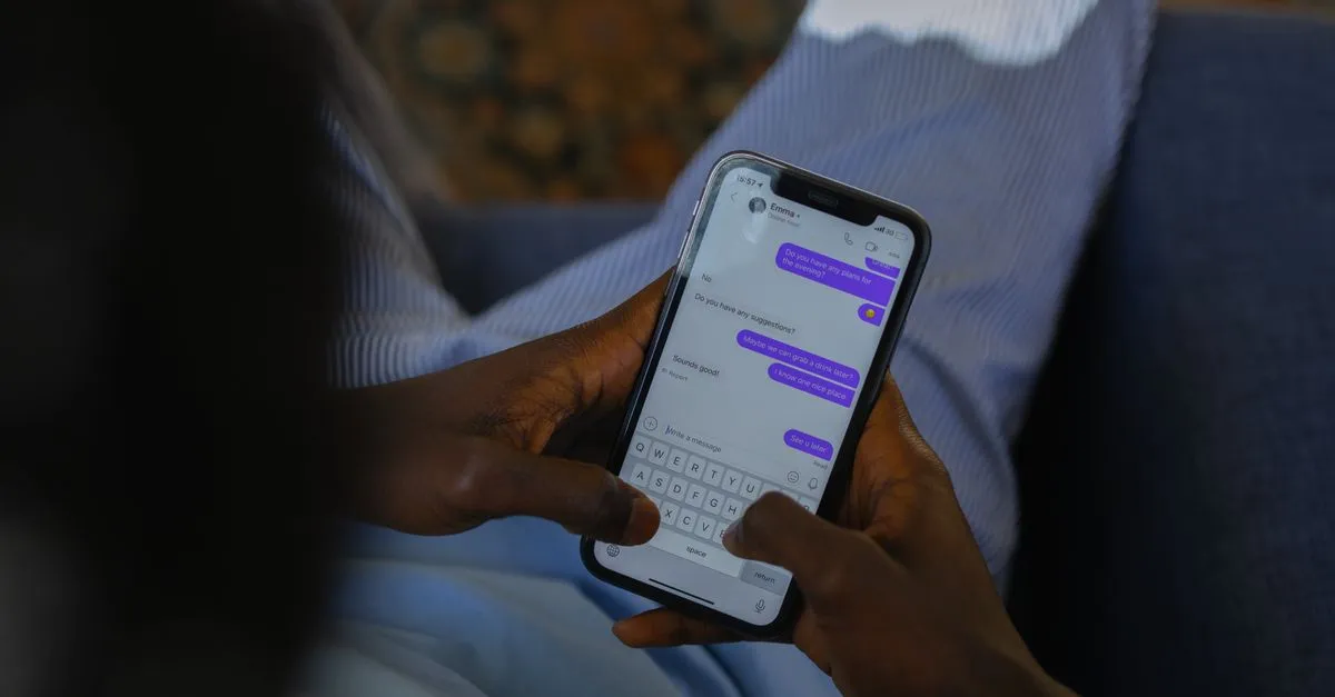 Hands typing a chat message on a smartphone screen with emoji in the keyboard