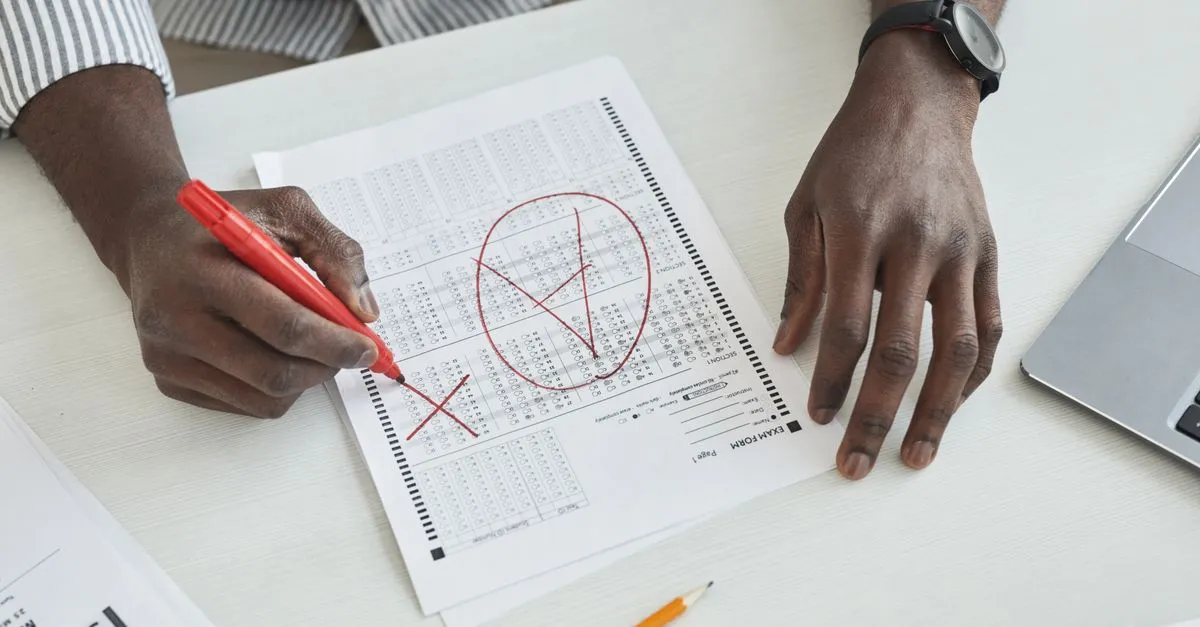 Teacher grading a stack of exam papers with a red pen to calculate test scores