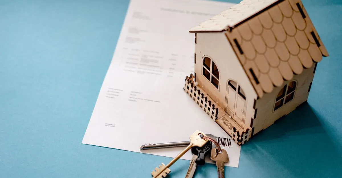 Small house model next to keys and a mortgage contract on a desk