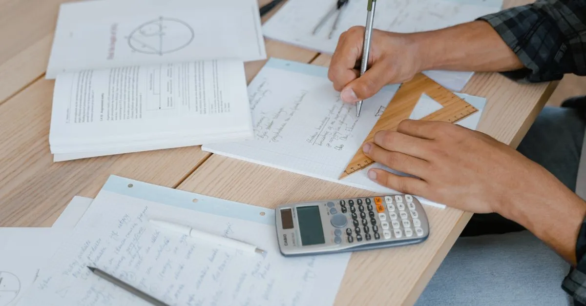Scientific calculator on a desk next to a notebook of handwritten equations and a pen