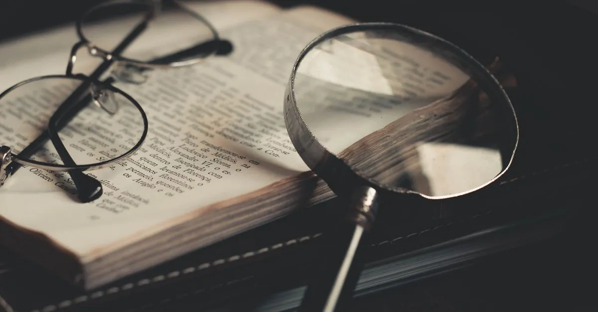 Magnifying glass held over the printed pages of an open book for word frequency analysis